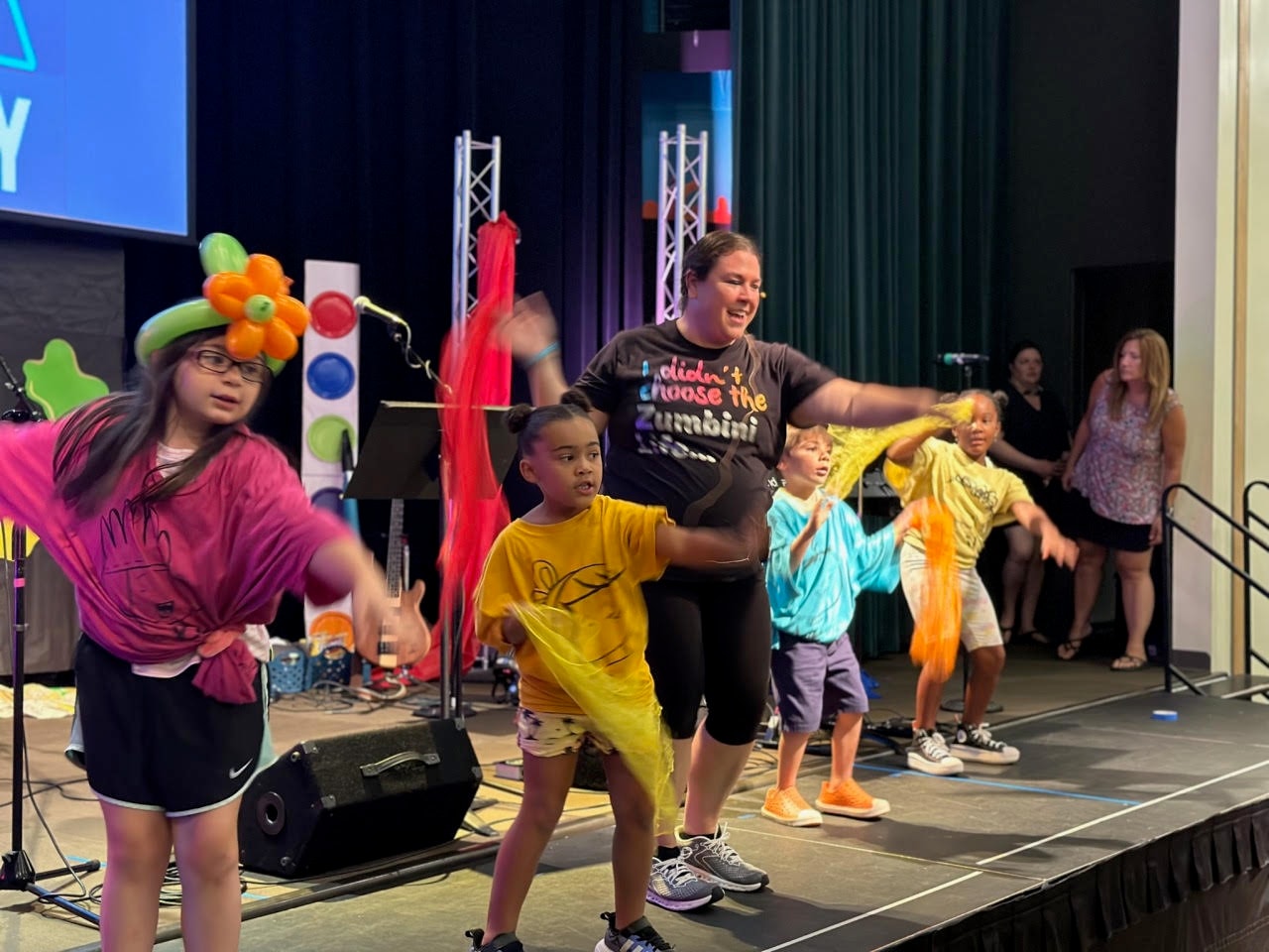 Miss Bri dancing on stage with children waving colorful scarves